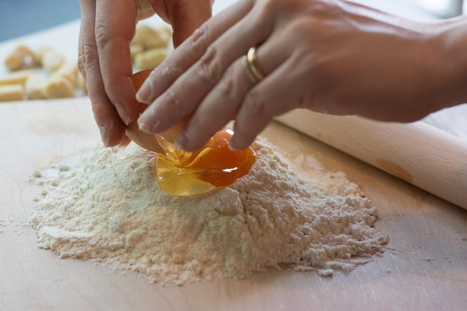 Hands cracking eggs into a well of flour on a wooden pasta board